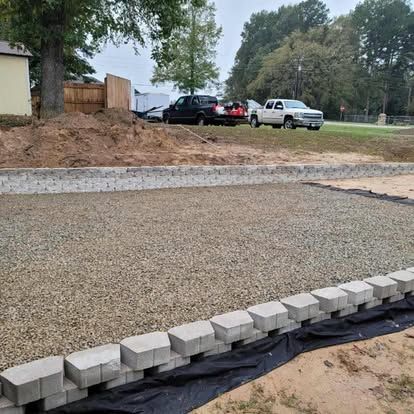 A rectangular area filled with gravel, bordered by concrete retaining wall blocks and landscape fabric in a yard.