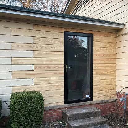 Exterior of a house showing a newly installed black storm door on a wall with mixed light wood and white lap siding.