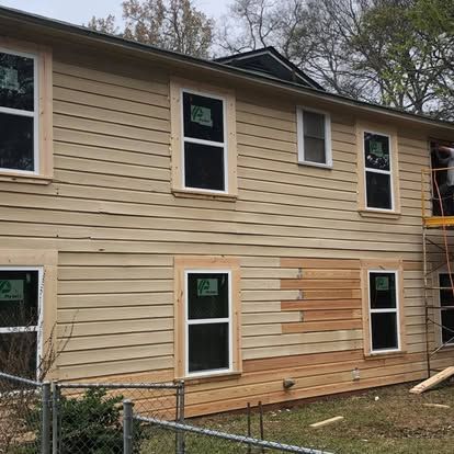 Two-story house exterior under renovation with tan siding, some sections being replaced with new wood boards.