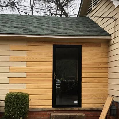 A partially renovated house exterior featuring new, light-colored horizontal siding next to an installed black screen door.