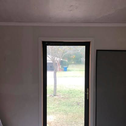 A view looking through a dark-framed glass door at a lawn, a tree, and a suburban house in the background.