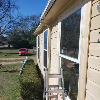 A step ladder placed against the exterior wall of a yellow home, next to two windows with new, unpainted wooden trim.