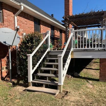 A set of wooden stairs with white railings leading up to a raised backyard deck attached to a brick house.
