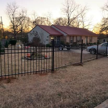 A house with a red metal roof sits behind a black metal fence on a wintery day at sunset.