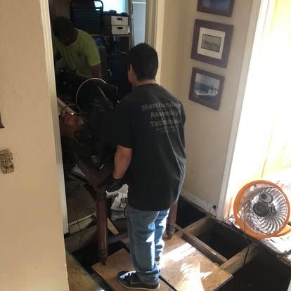 Two movers in uniform carefully maneuver a wooden table over an open floor section in a home.