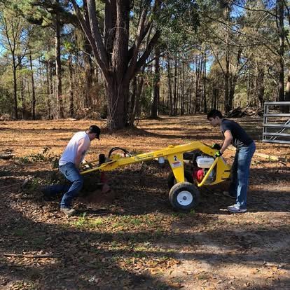 Two people operating a yellow log splitter in a wooded area.