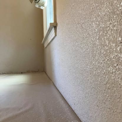 A side angle shows a textured, light-colored wall meeting a floor covered in a white protective sheet, near a window frame.