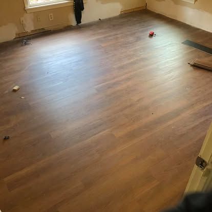 An empty room with light brown wood-look flooring and unfinished walls with baseboards.