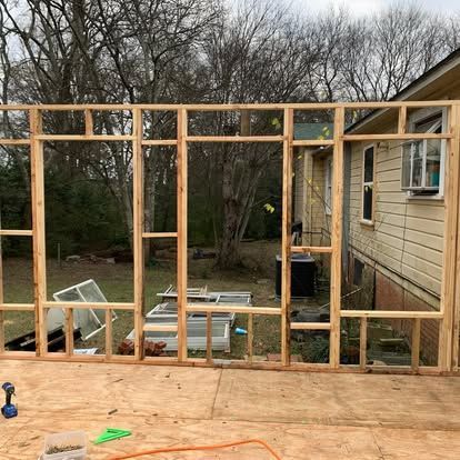Wooden wall frame for a home addition construction project, positioned in front of an existing yellow house.