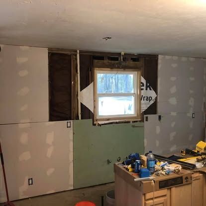An interior wall under construction with partially installed drywall, exposed framing, a window, and a kitchen island.
