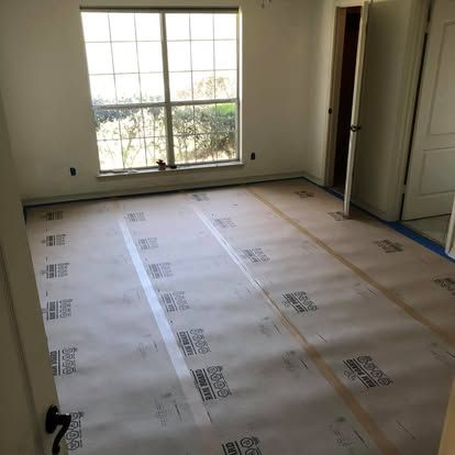 An empty bedroom with bare walls and window, showing flooring underlayment paper installed across the floor.