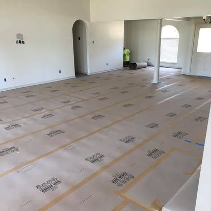 A bright, open room with beige protective paper taped across the floor, showing ongoing renovations.