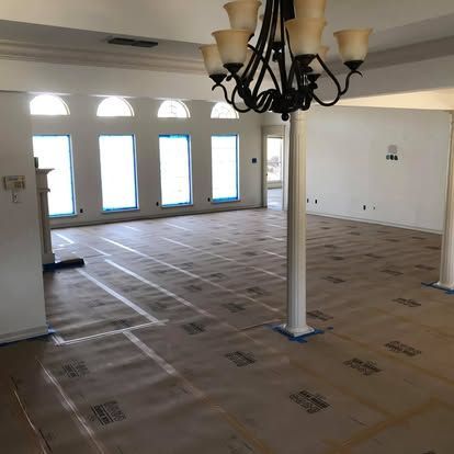 An interior room with white walls, arched windows, and a chandelier, with protective paper covering the floor.