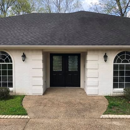 A front view of a white brick house with a dark roof, black double entry doors, and arched windows on both sides.