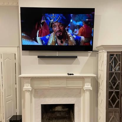 A television mounted above a fireplace mantle displays a scene from a movie featuring a character in blue attire.