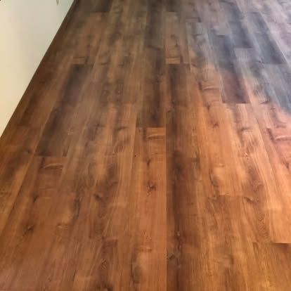 A close-up of dark brown wood-look laminate flooring panels installed with a staggered pattern along a white wall.