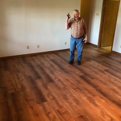 A person stands in a room with newly installed wood-look plank flooring, smiling and holding up a set of keys.