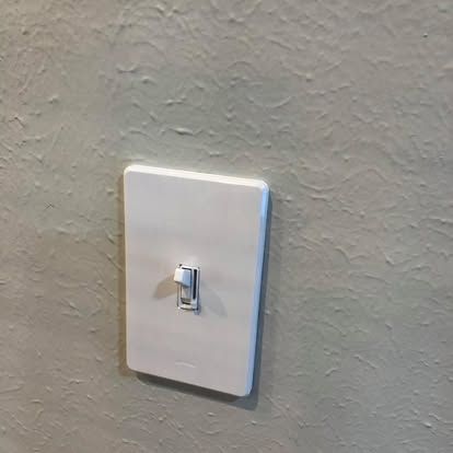 A white light switch mounted on a textured, light beige wall.