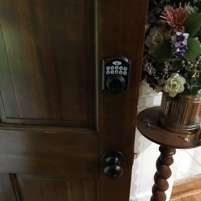 A dark wood door with a black digital keypad deadbolt and a round doorknob, next to a floral arrangement on a wood stand.