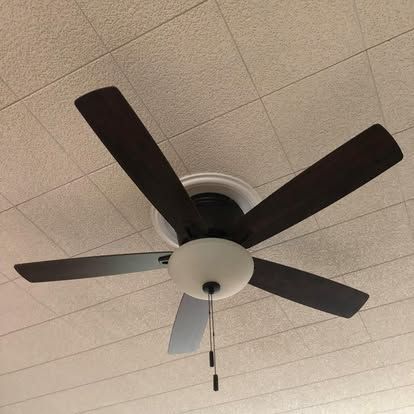 A five-blade ceiling fan with dark brown blades and a white glass dome light fixture, mounted on a textured white ceiling.
