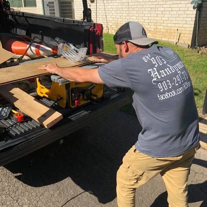 A person wearing a grey shirt and cap uses a table saw on a truck tailgate to cut a piece of wood.