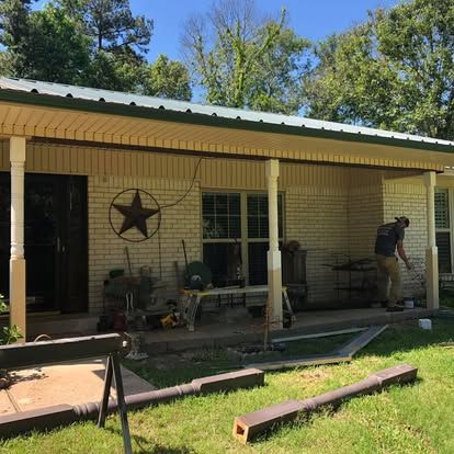 A person working on the porch of a brick house with a metal roof and a decorative metal star on the wall.