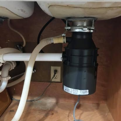 A garbage disposal unit connected to kitchen sink plumbing and an electrical outlet under a cabinet.