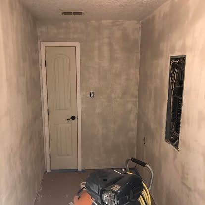 A narrow hallway with freshly primed drywall, a closed white door at the end, and an electrical panel in the right wall.