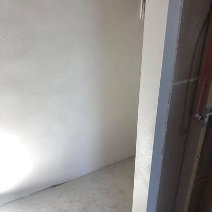 A white-walled room with a concrete floor, seen through a doorway with visible wood framing on the right side.