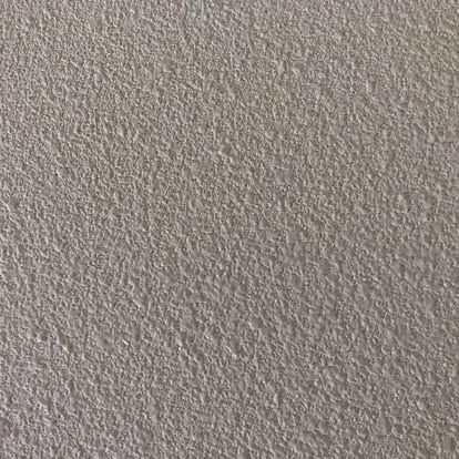 A close-up view of a uniform, light beige wall with a rough, textured stucco or plaster finish.