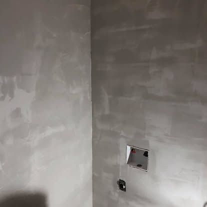 A corner of a room with unfinished drywall, featuring a recessed wall box and an electrical outlet.