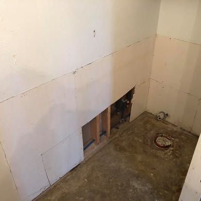 A small unfinished room with white drywall, exposed wall studs, and a circular pipe fitting in the concrete floor.