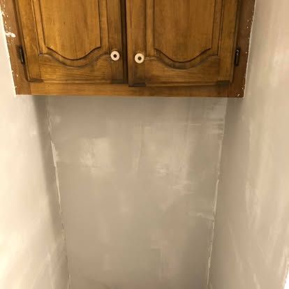 A light gray, freshly painted wall surface positioned directly below a set of light-brown wooden kitchen cabinets.
