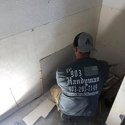 A repair worker in a branded gray t-shirt works on installing drywall panels in an unfinished room corner.