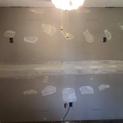 A gray drywall surface showing taped seams and patched screw holes in preparation for painting.