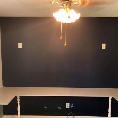 A dark-painted wall features a white desk surface with decorative legs, an overhead light fixture, and two light switches.