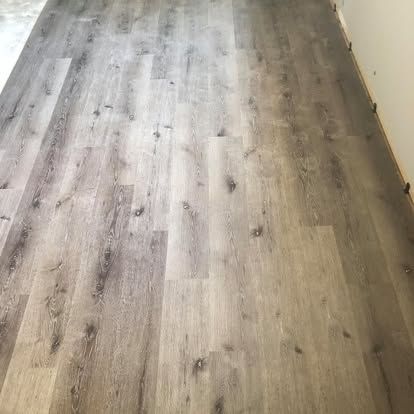 A close-up view of light gray, wood-look vinyl plank flooring installed in a room with light-colored walls.