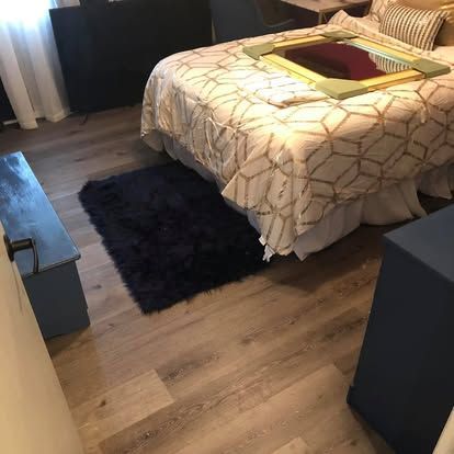A bedroom with light wood flooring, a bed featuring a geometric patterned quilt, a shaggy dark rug, and blue furniture.
