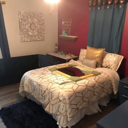 A bedroom with a bed featuring a geometric pattern quilt, gold pillows, and a large mirror resting on the bed surface.