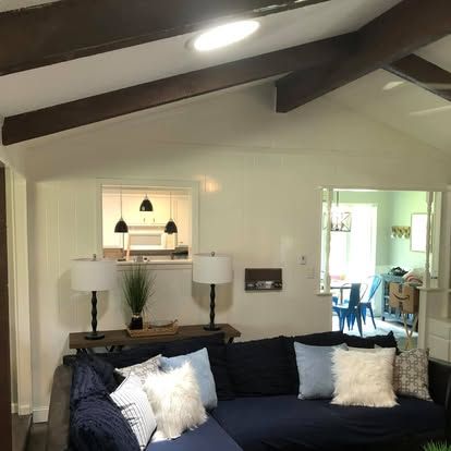 A living room with a navy blue sofa featuring light pillows, two table lamps on a wood console, and a view into a dining room.