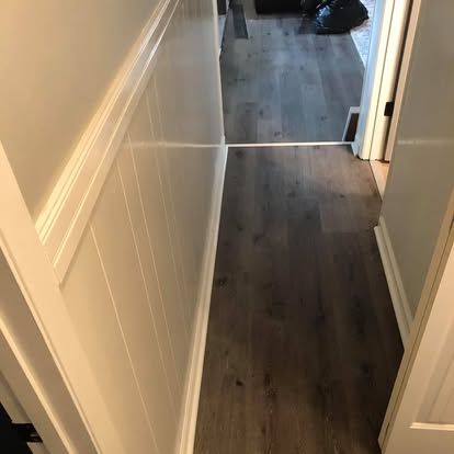 A hallway with vertical white wainscoting on the left wall and dark wood-look plank flooring.