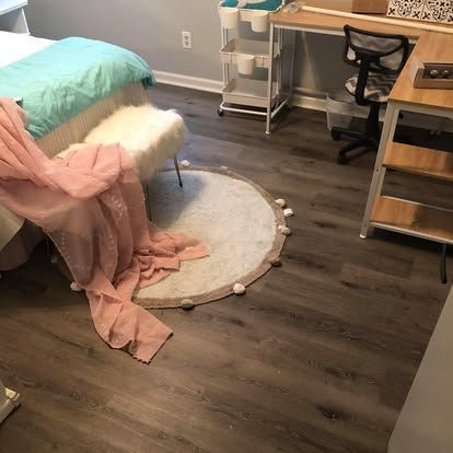 A bedroom with a light blue bed, a faux fur stool, a pink throw blanket, a round rug, and a desk with a rolling chair.