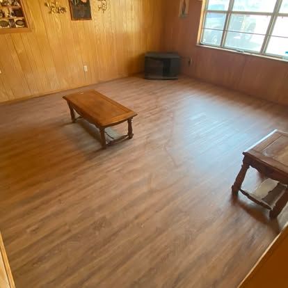 A wood-paneled room with light wood-look flooring, a coffee table, a side table, and a small TV stand near a window.