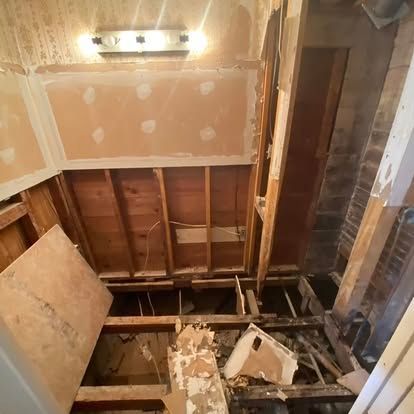 A bathroom under construction with exposed wooden wall studs, floor joists, and a section of drywall removed.