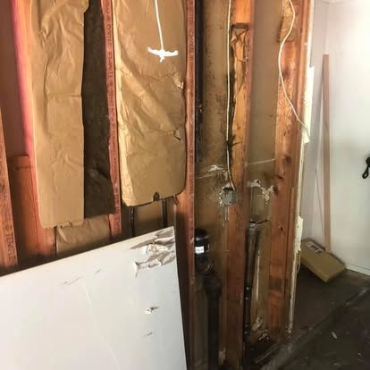 Interior wall framing with exposed wood studs, insulation, electrical wiring, and plumbing pipes visible behind drywall.