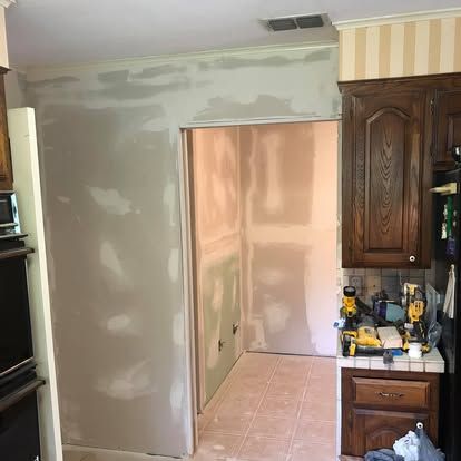 A room undergoing renovation with freshly applied drywall compound on the walls and an open doorway leading to a hallway.