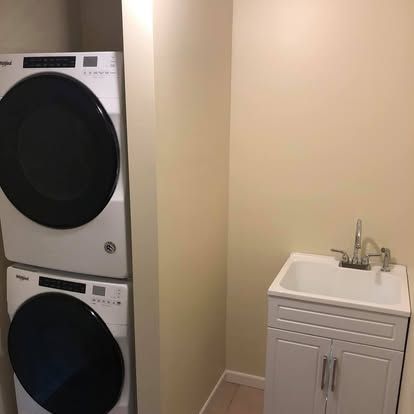 White stackable washer and dryer next to a white laundry sink in a light-walled utility room.