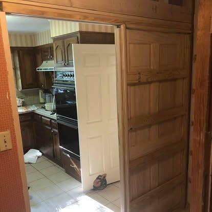 A view looking through a wooden door frame into a kitchen with wooden cabinets, a built-in oven, and tiled flooring.