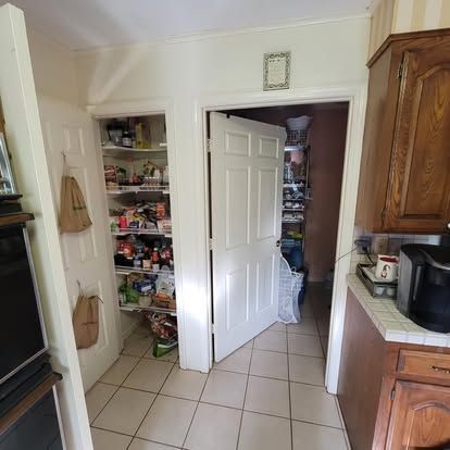 A kitchen pantry with open shelving full of food, next to an open white door leading to a room with stacked items.