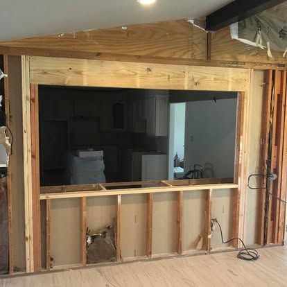 A partially framed interior wall opening or pass-through with raw wooden studs, drywall backing, and visible wires.